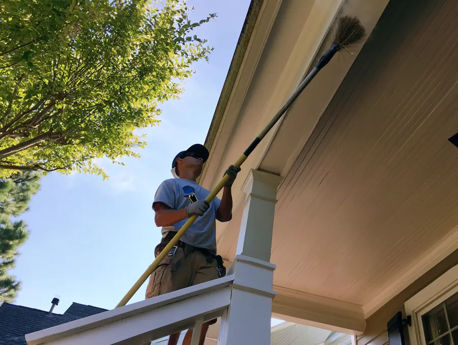 Technician sweeping webs from the eaves of a front porch